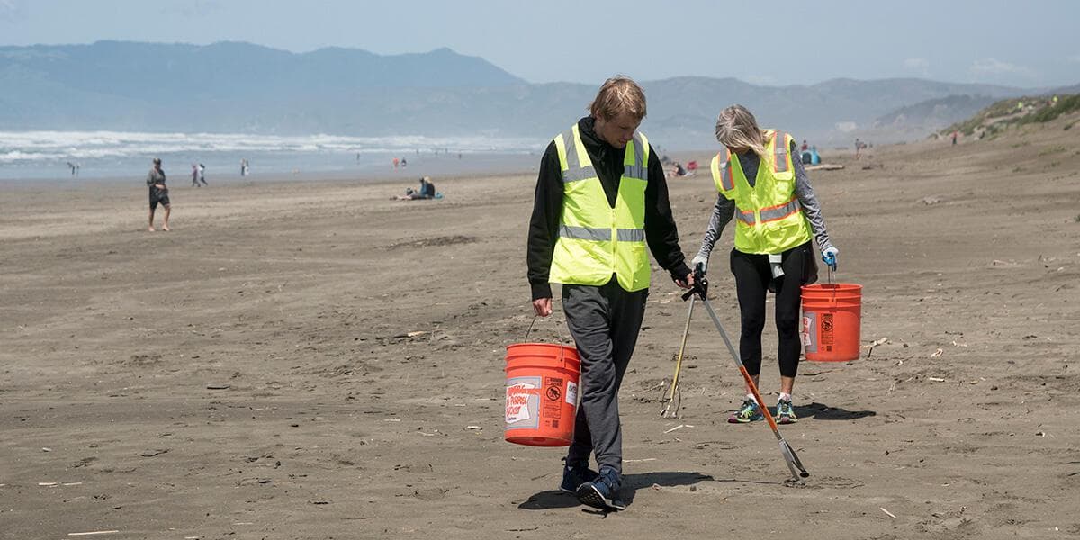 Two volunteers use a litter picker to pick up trash on ocean beach